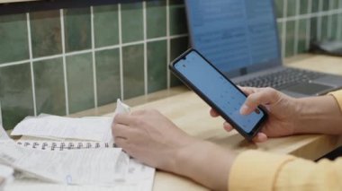 Tanınmayan süpermarket muhasebecisinin fişleri analiz etmesi ve gün sonunda mağaza gelirlerini sayarken akıllı telefondan hesaplamalar yapması.