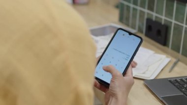 Marketin tanınmayan sahibinin omuz üstü fotoğrafı akıllı telefondaki hesap makinesi uygulamasını kullanarak vardiya üstüne dükkan gelirlerini sayarken.