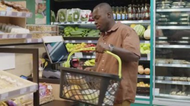 Orta boy Afro-Amerikan genç bir adamın yiyecek ürünlerini tarayıcıyla çalarken modern süpermarkette sağlıklı yiyeceklerle kendini kontrol ederken görüntüsü.