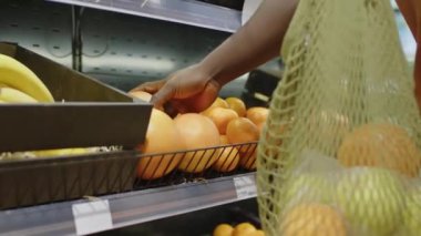 Tanımlanamayan bir erkek alıcının marketteki raftan olgun pomelo alıp sürdürülebilir çevre dostu alışveriş ağına koyduğu görüntüler.