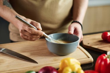 Mutfak masasının yanında durmuş çırpılmış yumurta çırpan tanınmamış bir adamın yakın çekimi.