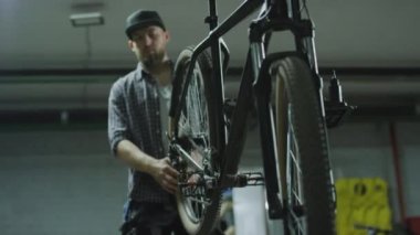Tamirci atölyede asılı duran bisikleti döndürüyor, sonra da tamir atölyesindeki tornavidayla tamir ediyor.