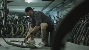 Tamirci garajda oturuyor, tekerleği pompalıyor ve bisikleti tamir ederken kontrol ediyor.