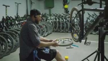 Bisiklet tamircisinde çalışırken, kulaklıklı tamirci sandviç paketini açıyor ve yemek yiyor.