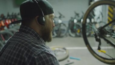 Kulaklıklı genç adam öğle arasında bisiklet tamirhanesinde müzik dinliyor ve sandviç yiyor.