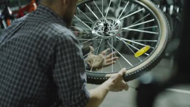 自転車のホイールを保持している店員を修理し タイヤとリムをチェックし ガレージで修理しながらツールを使用する — ストック動画
