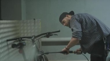 Garajda yıkadıktan sonra erkek tamirci bisikletini temiz suyla duruluyor.