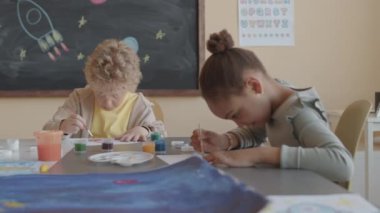 Kağıt üzerinde resim yapan ve ilkokulda resim dersi alırken konuşan çok ırklı çocuklardan oluşan bir grup.