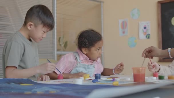 小学艺术课上 非洲裔美国女孩和亚裔男孩带着粉笔在纸上作画 微笑着聊天 非常可爱 — 图库视频影像