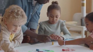 Siyahi öğretmen ve bir grup çok ırklı ilkokul öğrencisi resim dersi sırasında gezegende mum boya kalemlerini kâğıda çizerken el çırpıyorlar.