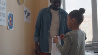 Afrika kökenli Amerikalı erkek öğretmen küçük kıza sınıfta duvara uzay roketi çizmesi için yardım ediyor.