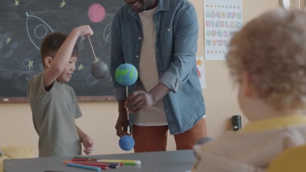 Маленький Азиатский Мальчик Держит Модель Планеты Отвечает Вопросы Чернокожего Учителя — стоковое видео