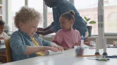 İlkokulda sınıfta masa başında uzay roketi yaparken kıvırcık sarı saçlı kâğıtlı küçük çocuk.