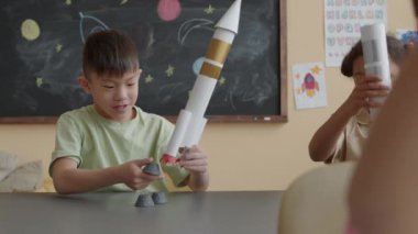 Küçük Asyalı çocuk, ders sırasında okul masasında otururken Afrika kökenli Amerikalı kızla roket yapıp oynuyordu.