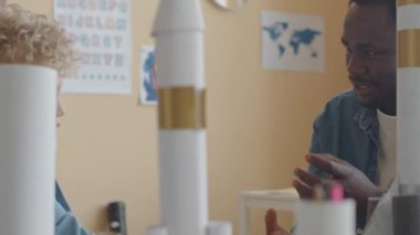 Sarı kıvırcık saçlı, Afrikalı Amerikan öğretmenini dinleyen ve okulda ders sırasında uzay roketini öğrenen küçük beyaz çocuk.