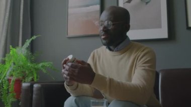Orta boy Afro-Amerikan bir adamın kanepede oturup hapları incelediği ve klinikte psikoterapistle konuştuğu bir fotoğraf.