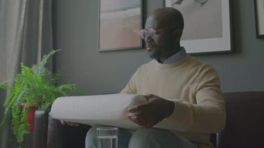 Uyku kliniğinde kanepede oturan Afrikalı Amerikalı erkek hasta ve doktorun tavsiye ettiği ortopedik yastığı muayene ediyor.
