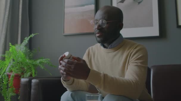 Μέτριο Πλάνο Του Αφροαμερικανού Άνδρα Κάθεται Στον Καναπέ Εξέταση Χάπια — Αρχείο Βίντεο