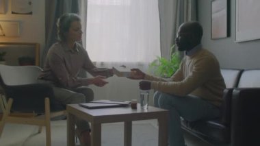 Orta yaşlı kadın uyku doktoru somnoloji kliniğinde tıbbi danışmanlık sırasında bir kutu bitki çayı veriyor ve Afrikalı Amerikalı hastayla konuşuyor.