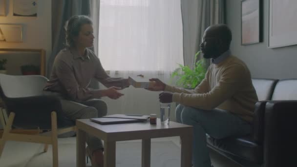 Lekarz Średnim Wieku Podający Pudełko Herbaty Ziołowej Rozmawiający Afroamerykańskim Pacjentem — Wideo stockowe