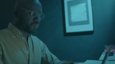 Siyah adamın karanlık yatak odasında oturduğu ve fazla mesai yaparken dizüstü bilgisayarda yazarken ya da gece uyku bozukluğundan acı çekerken görüntüsünü aşağı eğ.