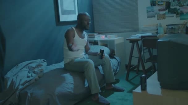 Hombre Afroamericano Sentado Cama Habitación Oscura Sosteniendo Bebida Energética Apoyando — Vídeo de stock