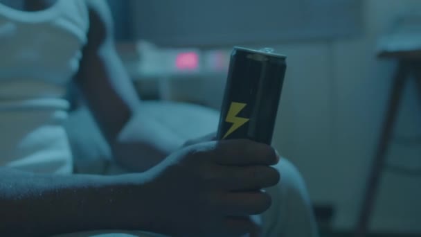 一个无法辨认的黑人男子深夜坐在床上 手里拿着能量饮料 看电视 拍了近照 — 图库视频影像