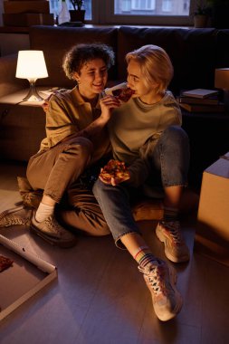 Yeni dairelerinde taşındıktan sonra pizza yiyen lezbiyen kızların dikey görüntüsü.