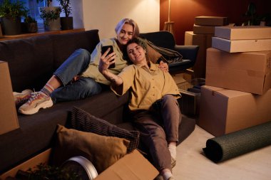 Arkadaşlar kanepede dinleniyor ve akıllı telefondan video izliyorlar. Yeni bir dairede dinleniyorlar.