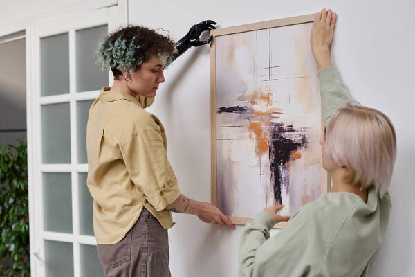 Lesbian couple decorating their room, they hanging modern painting on the wall
