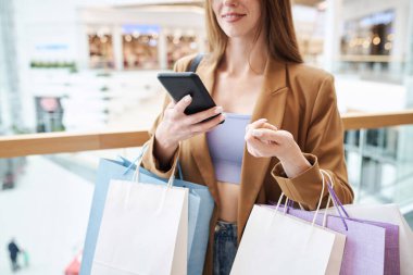 Elinde cep telefonu ve alışveriş merkezinde poz veren kağıt poşetler tutan kimliği belirsiz bir kadın.