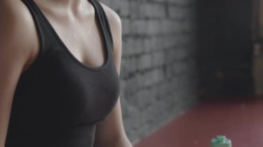 Spor salonundaki yorucu antrenmanlardan sonra terini havluyla silip silip siyah çatı katı tarzı tuğla duvara yaslanan genç, yorgun ve aktif bir kadın.