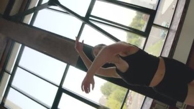 Siyah aktif giysili, tutkulu, kısa saçlı bir kadının panoramik pencereli geniş çatı katı stüdyosunda dans ederken çekildiği kaleydoskop fotoğrafı.