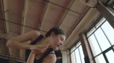 Çatı katı tarzı dans stüdyosunda serbest dans ederken, vücutlarıyla garip hareketler yapan iki esnek kızın düşük açılı ark çekimi.