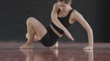 Genç yetenekli, beyaz ayaklı, dar siyah etekli bluz giyen ve stüdyoda kırmızı parke zeminde dans eden bir kadın.