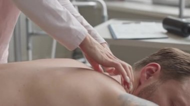 Klinikteki kanepede yatan erkek hastanın sırtına ve omuzlarına masaj yapan kadın masaj terapisti.
