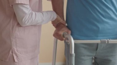 Klinikte rehabilitasyon sırasında kadın fizyoterapistin yardımıyla erkek hastaların yürüyüş çerçevesini kullanırken yakın plan çekimleri.