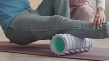 Kadın doktorun, erkek hastaya egzersiz minderinde yardım ederken ve baldır masajı yaparken, fizyoterapi kliniğinde köpüklü rulo çekimini yapın.