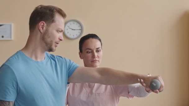 Férfi Nevelés Súlyzó Segítségével Női Fizioterapeuta Klinikán Miközben Rehabilitációs Gyakorlatok — Stock videók