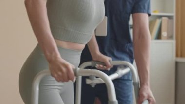 Yüksek açılı fizyoterapistin rehabilitasyon seansı sırasında kadının yürüme sahnesiyle yürümesine yardım ettiği görüntüler.