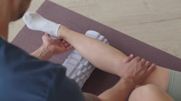 临床康复训练期间 专业理疗师在运动垫子上用泡沫辊按摩小牛犊 协助女病人的肩上照一张相 — 图库视频影像