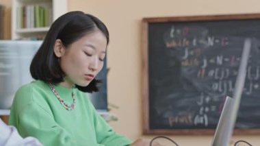 Genç Asyalı kız öğrenci dizüstü bilgisayar kullanıyor ve üniversitedeki programlama dersi sırasında Afrikalı Amerikalı grup arkadaşına bilgisayar kodlarını soruyor.