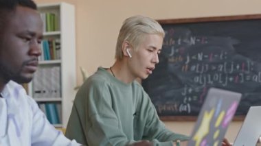 Kablosuz kulaklıklı genç Asyalı öğrenci üniversitedeki programlama dersi sırasında dizüstü bilgisayarında müzik dinliyor ve şarkı söylüyor.