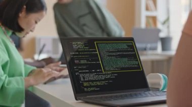 Üniversitede programlama dersinde masa başında otururken dizüstü bilgisayarda bilgisayar kodları yazan bir kız öğrencinin omuz üstü fotoğrafı.