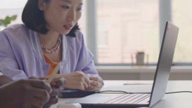 Genç Asyalı kız ve siyah adam dizüstü bilgisayarı gösteriyorlar ve lisede programlama dersinde çift olarak çalışırken tartışıyorlar.