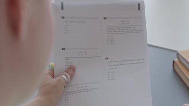 Bilgisayar bilimi dersinde masa başında oturmuş sınav sorularını okuyan üniversiteli bir kızın omuz üstü fotoğrafı.