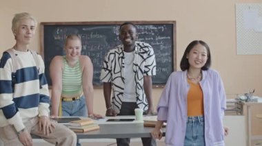 Üniversitedeki bilgisayar bilimi dersinde masanın etrafında durmuş kameraya bakıp gülümseyen genç öğrencilerin grup portresi.