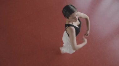 Geniş, esnek, beyaz, siyah bluzlu bir kadın ve geniş dans stüdyosunun kırmızı parkesi üzerinde dans eden beyaz koşucular.