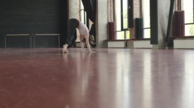 İyi eğitilmiş beyaz kadın rahat spor kıyafetleriyle tavan arası dans sınıfında kırmızı parke üzerinde serbest dans ediyor.