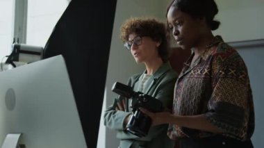 Genç kadın fotoğrafçı ve kreatif direktör kamera ve bilgisayardan fotoğrafları kontrol ediyor ve stüdyoda çekim gününü tartışıyorlar.